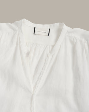 Close-up of a white blouse with a gathered V-neckline, scalloped trim, and a visible neck label reading Colleen.