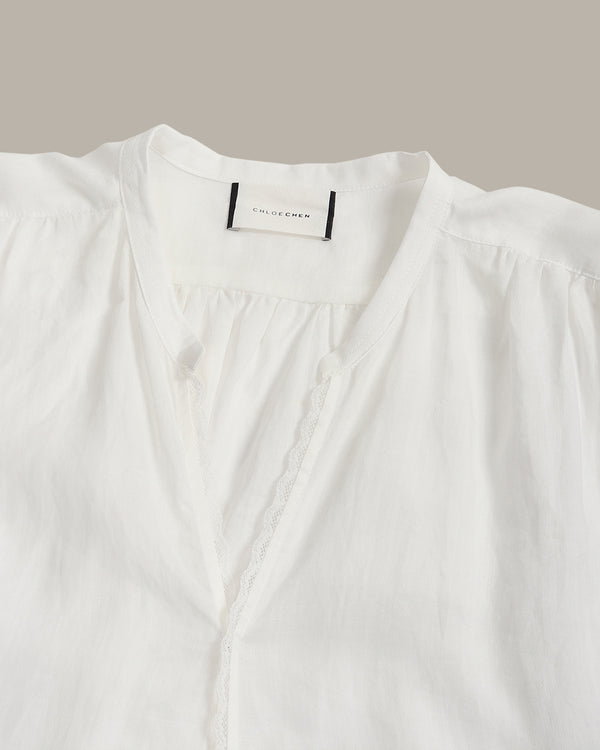 Close-up of a white blouse with a gathered V-neckline, scalloped trim, and a visible neck label reading Colleen.