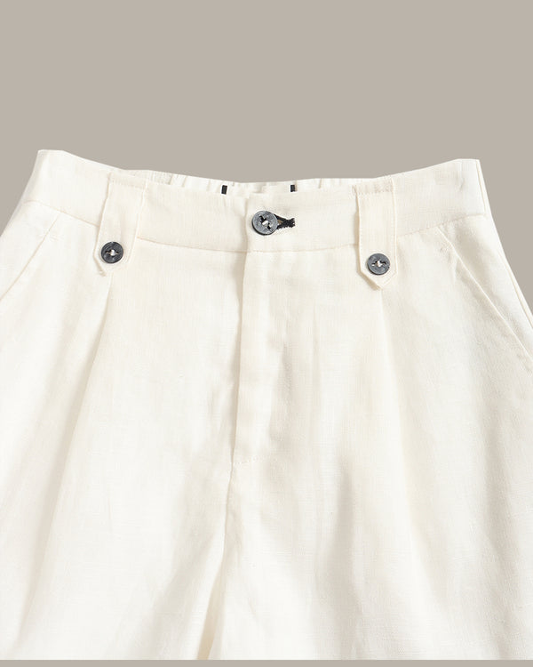 Close-up of off-white pleated trousers showing the waistband, belt loops, and front button closure against a solid taupe background.