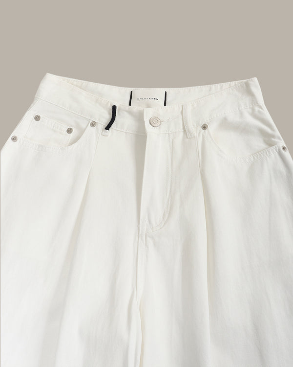 Close-up of white wide-leg denim pants showing the waistband, button closure, and front pockets against a solid taupe background.