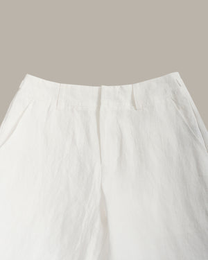 Close-up of white trousers showing the waistband, front fly, and side pockets against a solid taupe background.