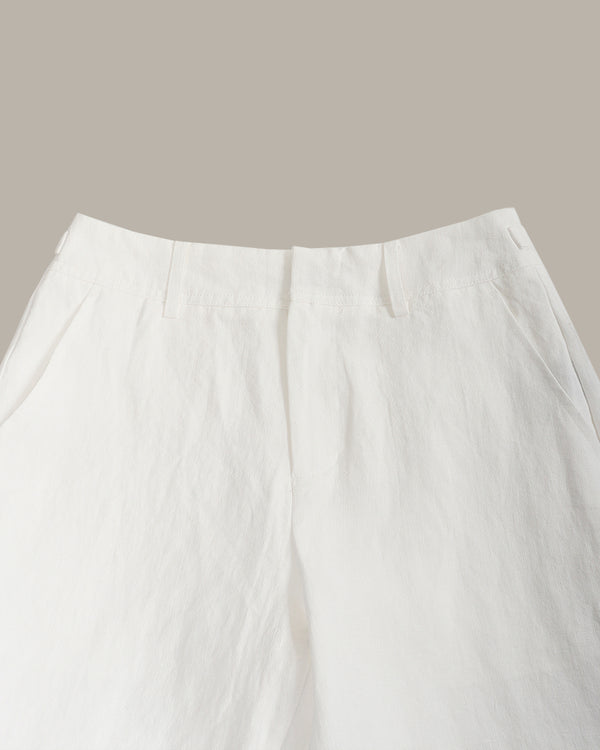 Close-up of white trousers showing the waistband, front fly, and side pockets against a solid taupe background.