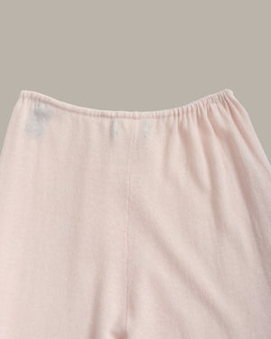 Close-up of a light pink fabric garment, showing the elastic waistband and upper front panel against a solid taupe background.