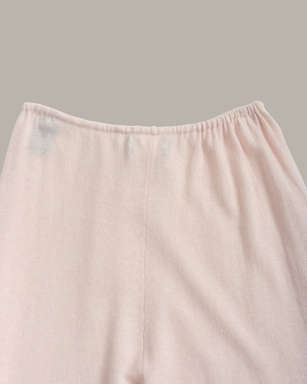Close-up of a light pink fabric garment, showing the elastic waistband and upper front panel against a solid taupe background.