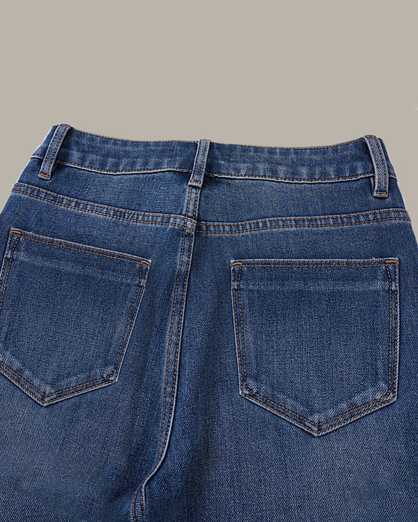 Close-up back view of blue denim jeans showing the waistband, belt loops, and back pockets against a solid taupe background.