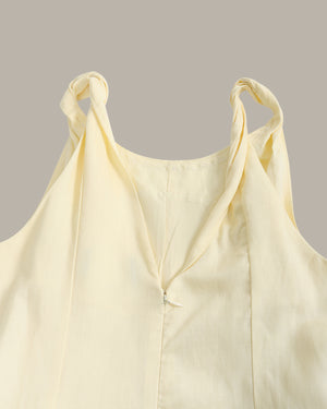 A pale yellow sleeveless top with twisted shoulder straps and a split V-neckline, shown against a solid taupe background.