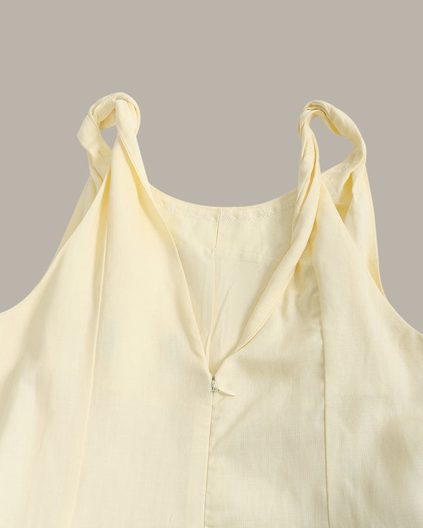 A pale yellow sleeveless top with twisted shoulder straps and a split V-neckline, shown against a solid taupe background.