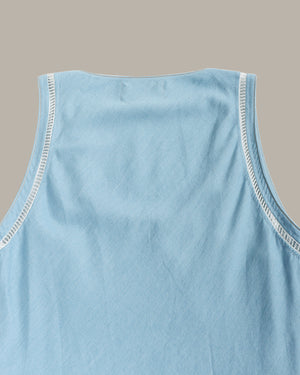 Close-up of a light blue sleeveless top showing the back neckline with white contrast stitching against a solid taupe background.