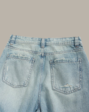 Light blue denim jeans with distressed details on a gray background