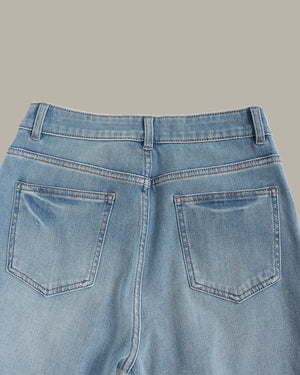 Close-up back view of light blue denim jeans showing the waistband, belt loops, and two rear patch pockets against a solid taupe background.