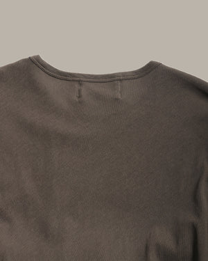 Close-up of the back of a dark brown crewneck t-shirt, showing the fabric texture and stitching details against a solid neutral background.