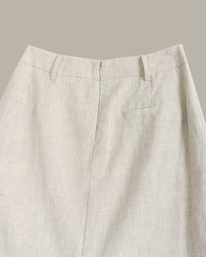 Close-up of the back waistband and upper back of light beige linen trousers, showing belt loops, a center back zipper, and a welt pocket on the right side against a solid taupe background.