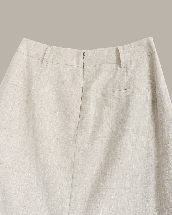 Close-up of the back waistband and upper back of light beige linen trousers, showing belt loops, a center back zipper, and a welt pocket on the right side against a solid taupe background.