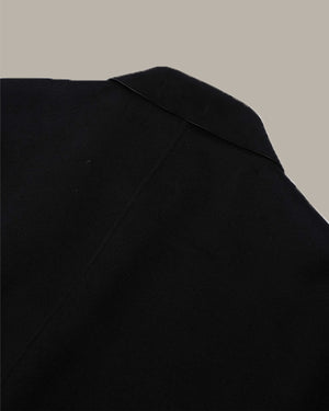 Close-up of a black garment, showing the shoulder and upper chest area with a subtle texture, set against a solid taupe background.