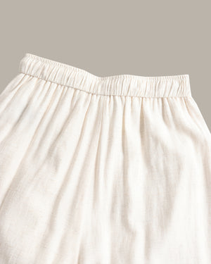 Close-up of a cream-colored, pants with an elastic waistband, set against a solid taupe background.