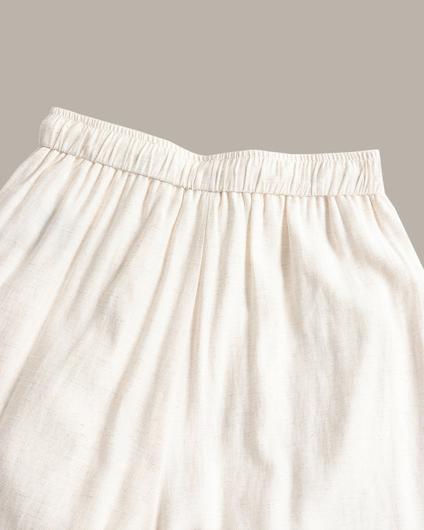 Close-up of a cream-colored, pants with an elastic waistband, set against a solid taupe background.