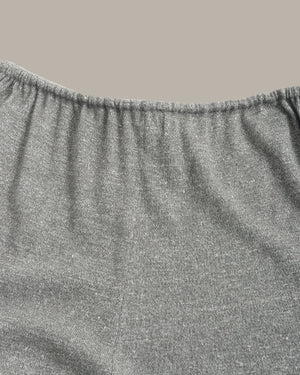 Close-up of a heather gray fabric garment, showing the elasticized waistband and textured knit material against a solid taupe background.