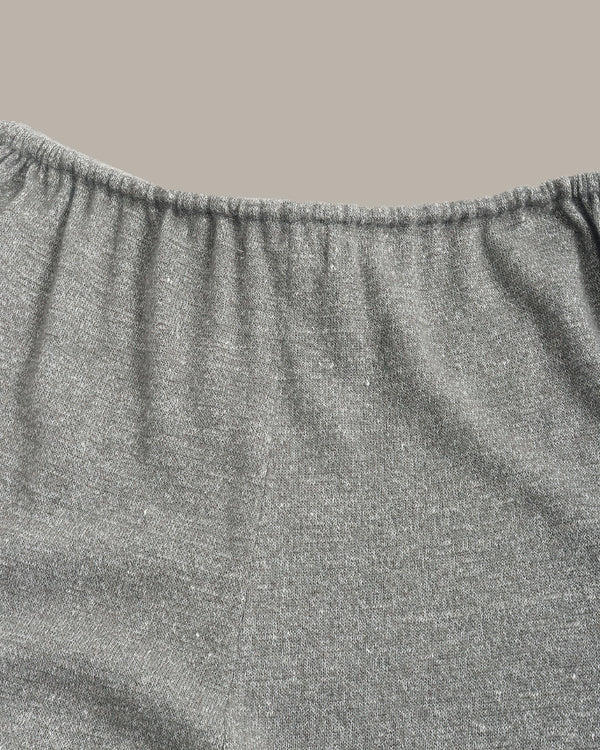 Close-up of a heather gray fabric garment, showing the elasticized waistband and textured knit material against a solid taupe background.