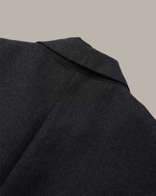 Close-up detail shot of a dark charcoal gray wool coat collar against a solid beige background.