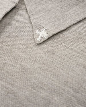 Close-up of a light gray knit polo shirt collar with a white embroidered cross logo on the point.