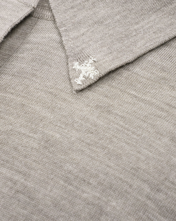 Close-up of a light gray knit polo shirt collar with a white embroidered cross logo on the point.