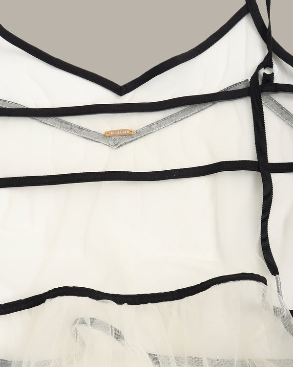 Close-up of a white dress with black straps and a brand label on a neutral background