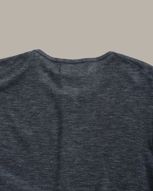 Close-up of the back of a dark heather gray crewneck shirt, showing the fabric texture and collar detail against a solid beige background.