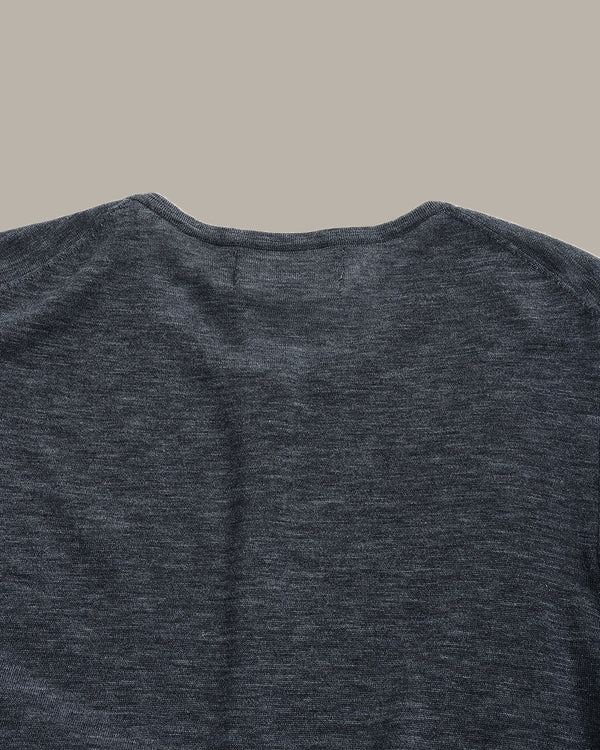 Close-up of the back of a dark heather gray crewneck shirt, showing the fabric texture and collar detail against a solid beige background.