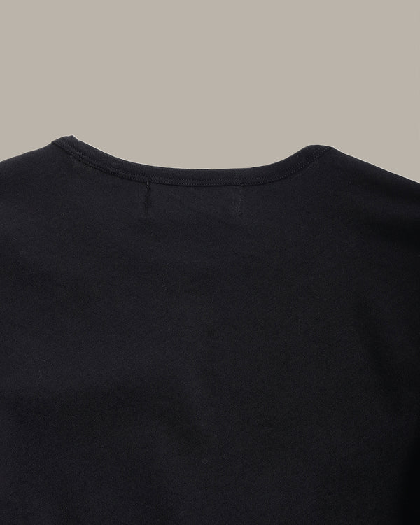 Close-up of the back neckline of a solid black crewneck t-shirt against a solid taupe-gray background.