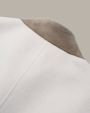 Close-up detail of a coat showing a smooth off-white body and a contrasting taupe suede-like lapel against a solid beige background.
