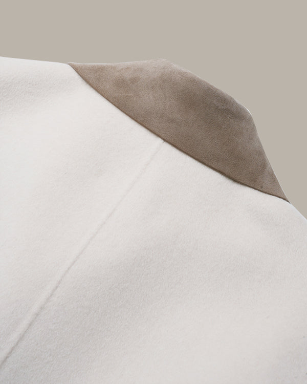Close-up detail of a coat showing a smooth off-white body and a contrasting taupe suede-like lapel against a solid beige background.