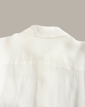 Close-up of a white cotton shirt showing the collar and upper back fabric texture against a solid taupe background.