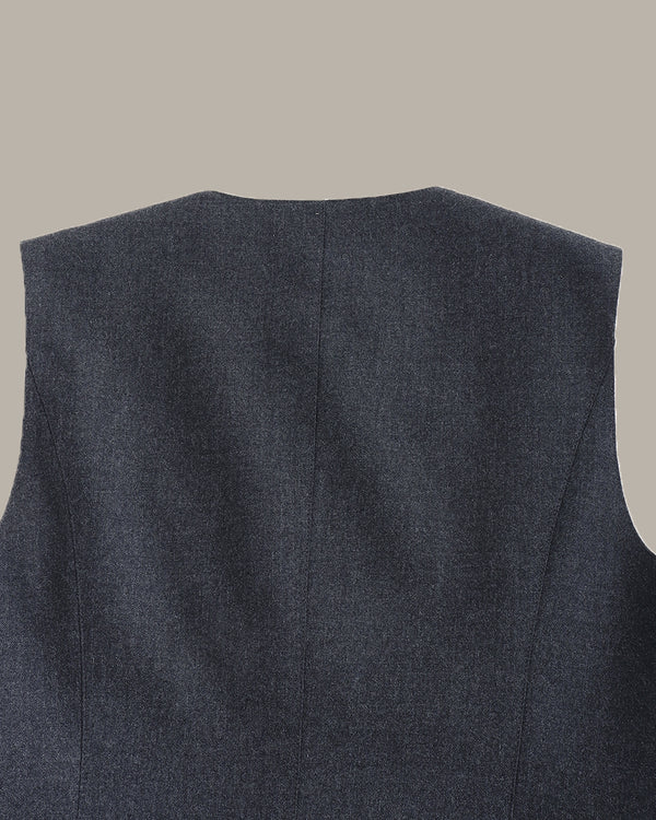Close-up of the back of a sleeveless dark gray textured vest or blazer, showing a centered seam and shoulder yokes against a plain warm gray background.