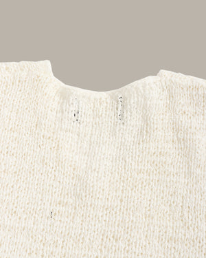 Close-up of a cream-colored textured knit garment, showing the fine ribbed fabric and a notched neckline against a solid taupe background.