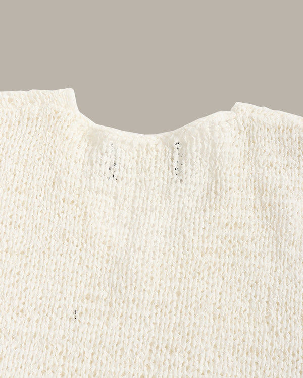 Close-up of a cream-colored textured knit garment, showing the fine ribbed fabric and a notched neckline against a solid taupe background.