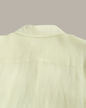 Close-up of a pale yellow-green shirt fabric showing the collar and upper chest area against a solid taupe background.