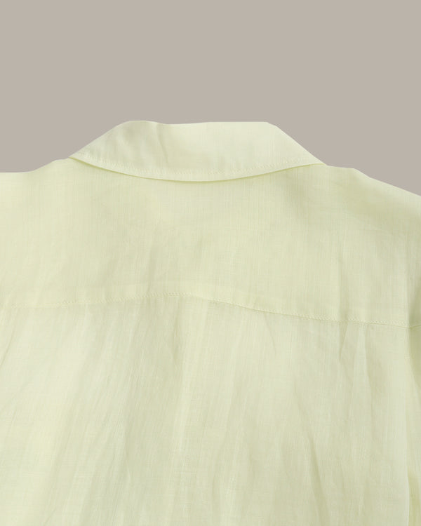 Close-up of a pale yellow-green shirt fabric showing the collar and upper chest area against a solid taupe background.