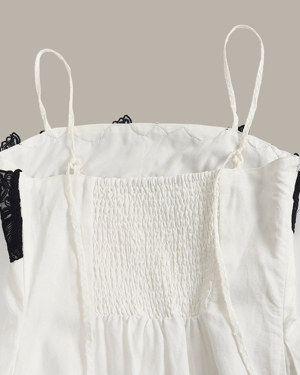 White smocked dress with black lace trim on a gray background