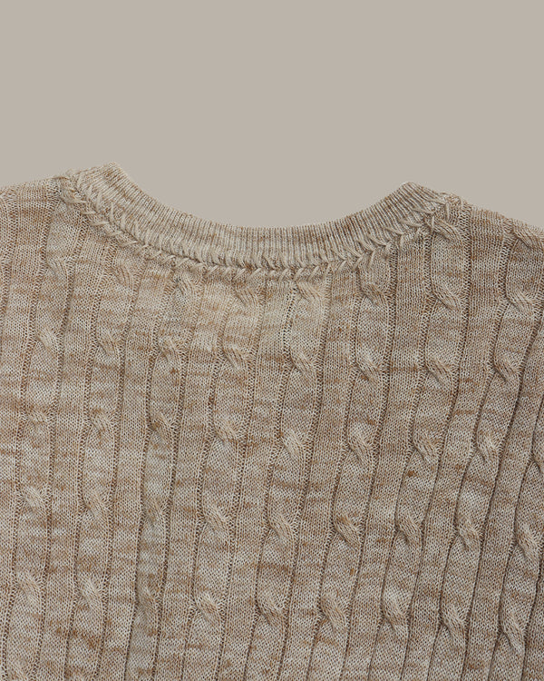 Close-up of a camel cable knit sweater on a light gray background