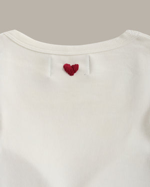 White ribbed sweater with a red heart design on a light gray background