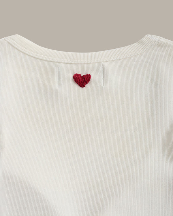 White ribbed sweater with a red heart design on a light gray background