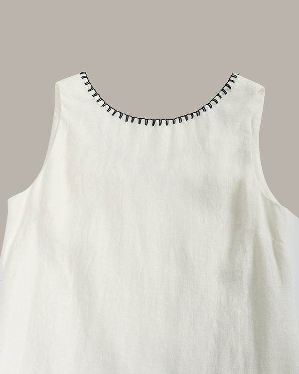 White sleeveless top with black embroidered neckline on a beige background