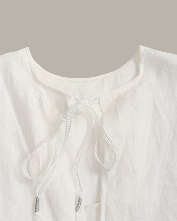 Close-up of a white textured linen blouse with a drawstring neckline, featuring a small silver bead accent on the cord.