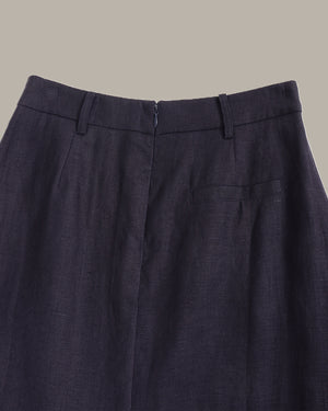 Close-up of the waistband of dark navy blue trousers, showing belt loops, front closure, and a side pocket against a solid beige background.