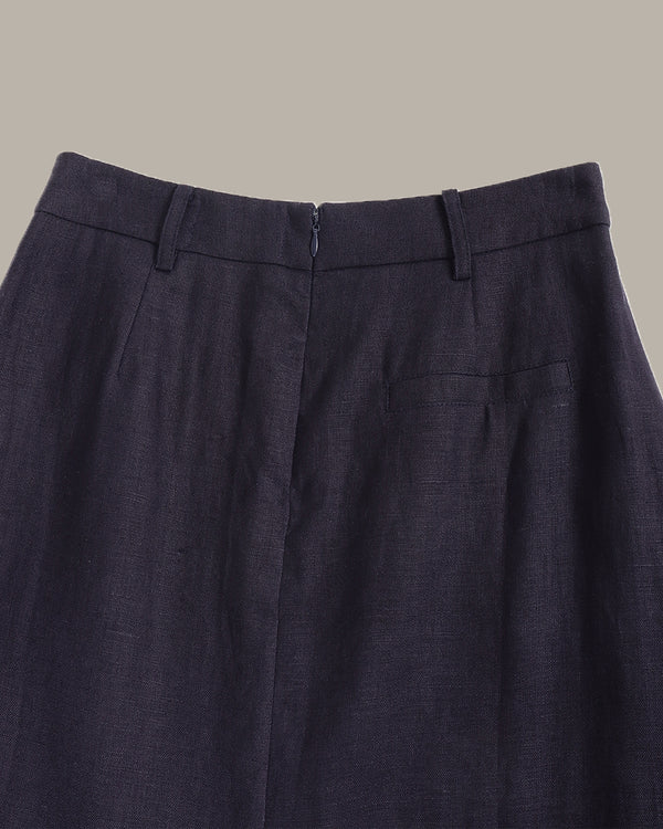 Close-up of the waistband of dark navy blue trousers, showing belt loops, front closure, and a side pocket against a solid beige background.