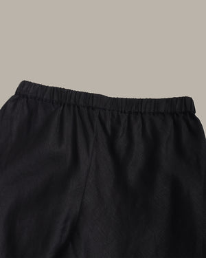 Close-up of black elastic-waist pants or shorts fabric against a plain warm gray background.
