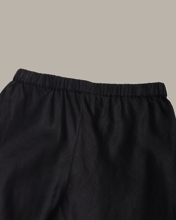 Close-up of black elastic-waist pants or shorts fabric against a plain warm gray background.