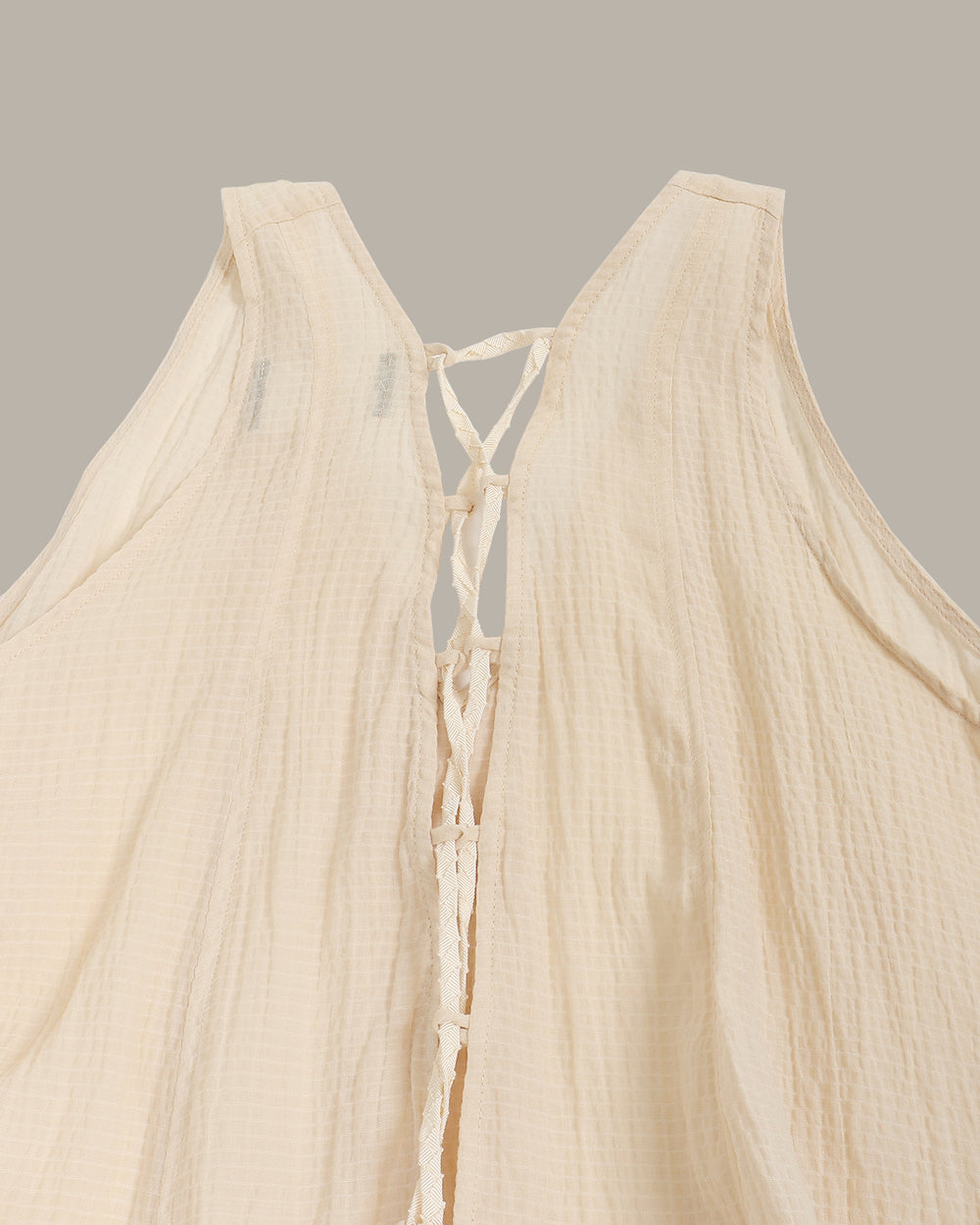 Beige sleeveless top with ruffled hem on a gray background