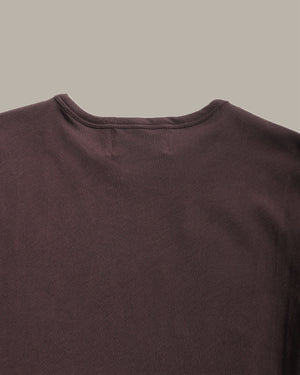 Close-up of a dark brown crew-neck t-shirt showing the collar and upper chest fabric against a solid light gray background.