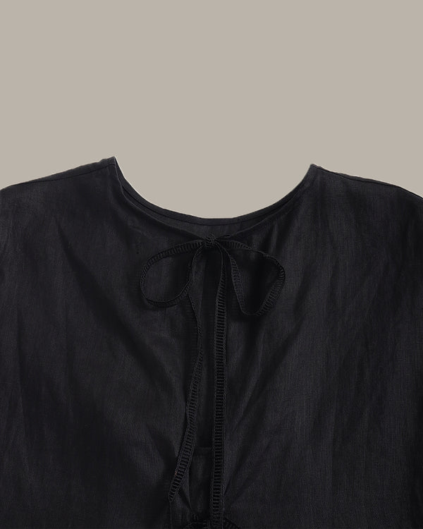 Close-up of a black top with a round neckline and a matching black ribbon tie at the front, shown against a solid taupe background.